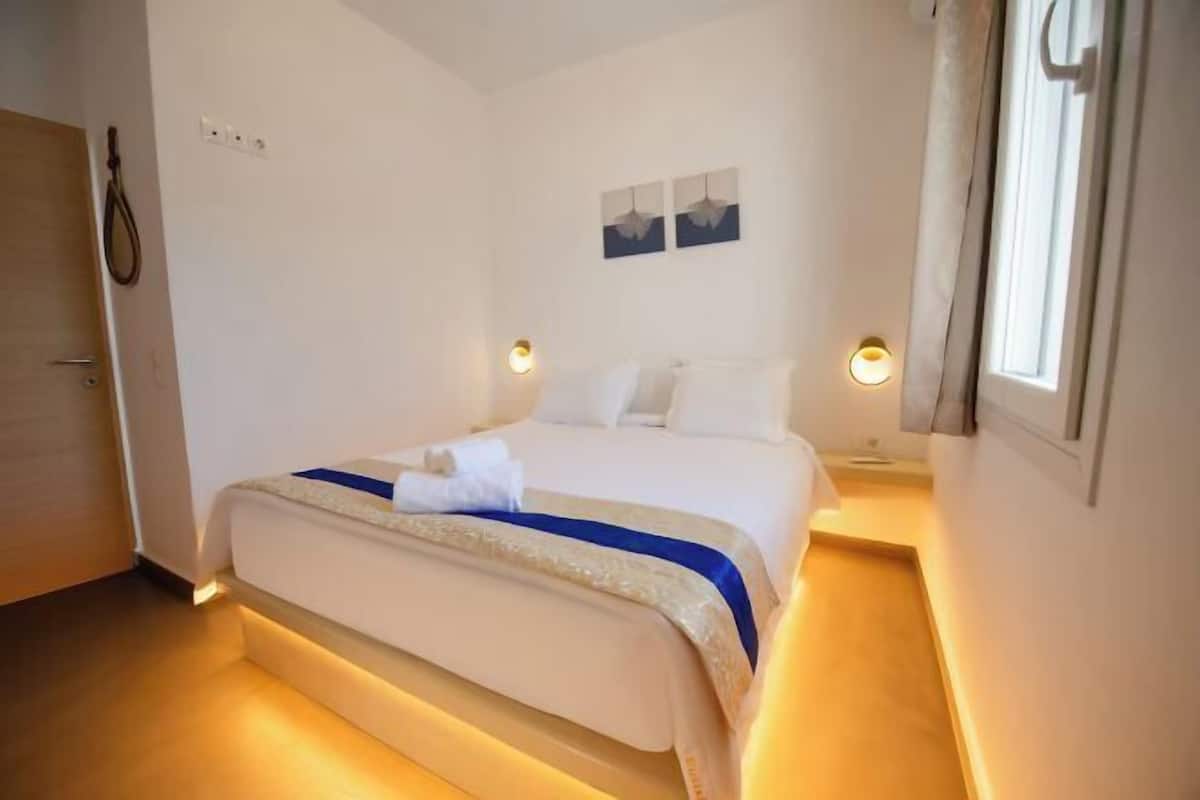 Een hotelkamer met een bed, nachtlampjes, een aan de muur hangend kunstwerk en een raam met gordijnen.