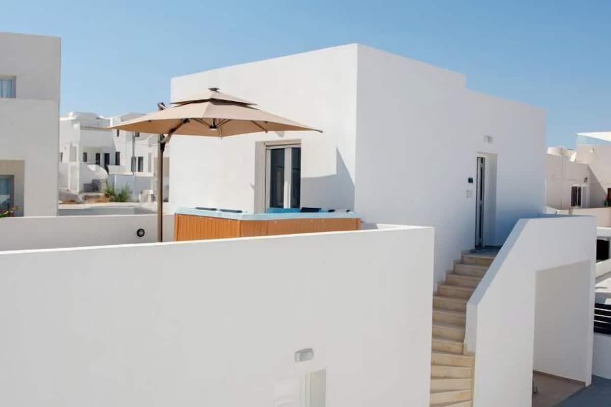 Een modern, wit gebouw met een houten terras en een beige parasol.