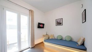 Een moderne kamer met een schuifdeur van glas, een ingebouwde bank met kussens, een aan de muur bevestigde televisie en een lijst met een afbeelding.