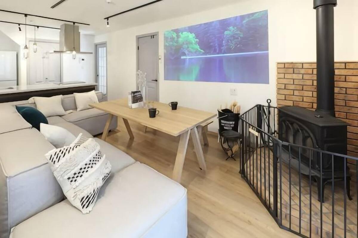 A modern living room with a sofa, a wooden table, a fireplace, and a projection screen.