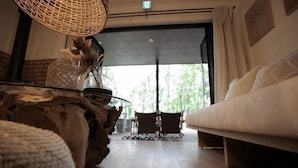 Ein Zimmer mit einer Couch, einem Couchtisch mit Dekoration, einem Korbstuhl und Blick durch ein großes Fenster.