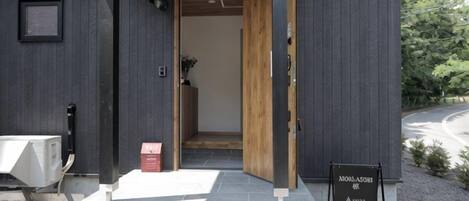 L’entrée d’un hôtel, avec une porte en bois, une enseigne et un petit espace extérieur aménagé avec des sièges.