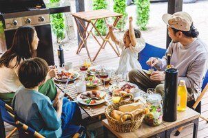 A family dining outdoors with a grill, table, and various food items.
