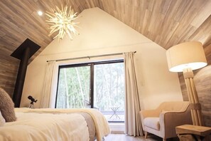 A bedroom with a large bed, a chair, a lamp, and a window with curtains.