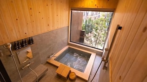 Ein Zimmer mit Holzwänden, einer Glaskonstruktion mit Whirlpool, einer Duschkabine und einem Fenster mit Blick auf Grünflächen.