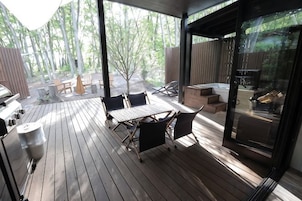 Terraza exterior con mesa y sillas, una parrilla y una puerta de vidrio que da a un área cubierta.