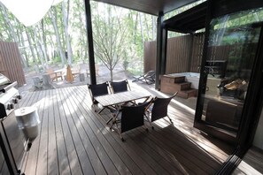 A covered outdoor patio with a table and chairs, a grill, and a glass door leading to a deck area. - [TV] Luxury adult secret base villa 120 ㎡ Sauna, stone bath, bonfire, BBQ [Mori building] (Miyota)