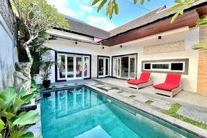 A modern poolside area with a clear pool, red lounge chairs, and a stone statue. - Enno Villa Sanur (Bali)