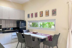 A modern kitchen with white cabinets, a black refrigerator, and a dining area with a table and four chairs. - Enno Villa Sanur (Bali)