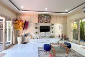 A modern living room with a flat-screen TV, a large potted plant, and a glass coffee table. - Enno Villa Sanur (Bali)