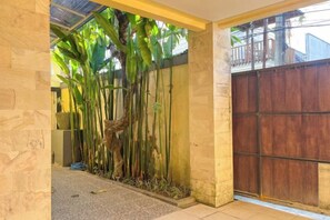 A covered outdoor area with a bamboo plant, a metal gate, and a stone wall. - Enno Villa Sanur (Bali)