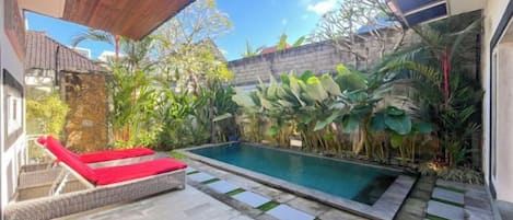 A swimming pool with a red lounge chair, surrounded by tropical plants, and a stone pathway.