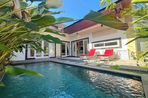 A swimming pool with a patio area, a covered seating area, and a building with large windows. - Enno Villa Sanur (Bali)
