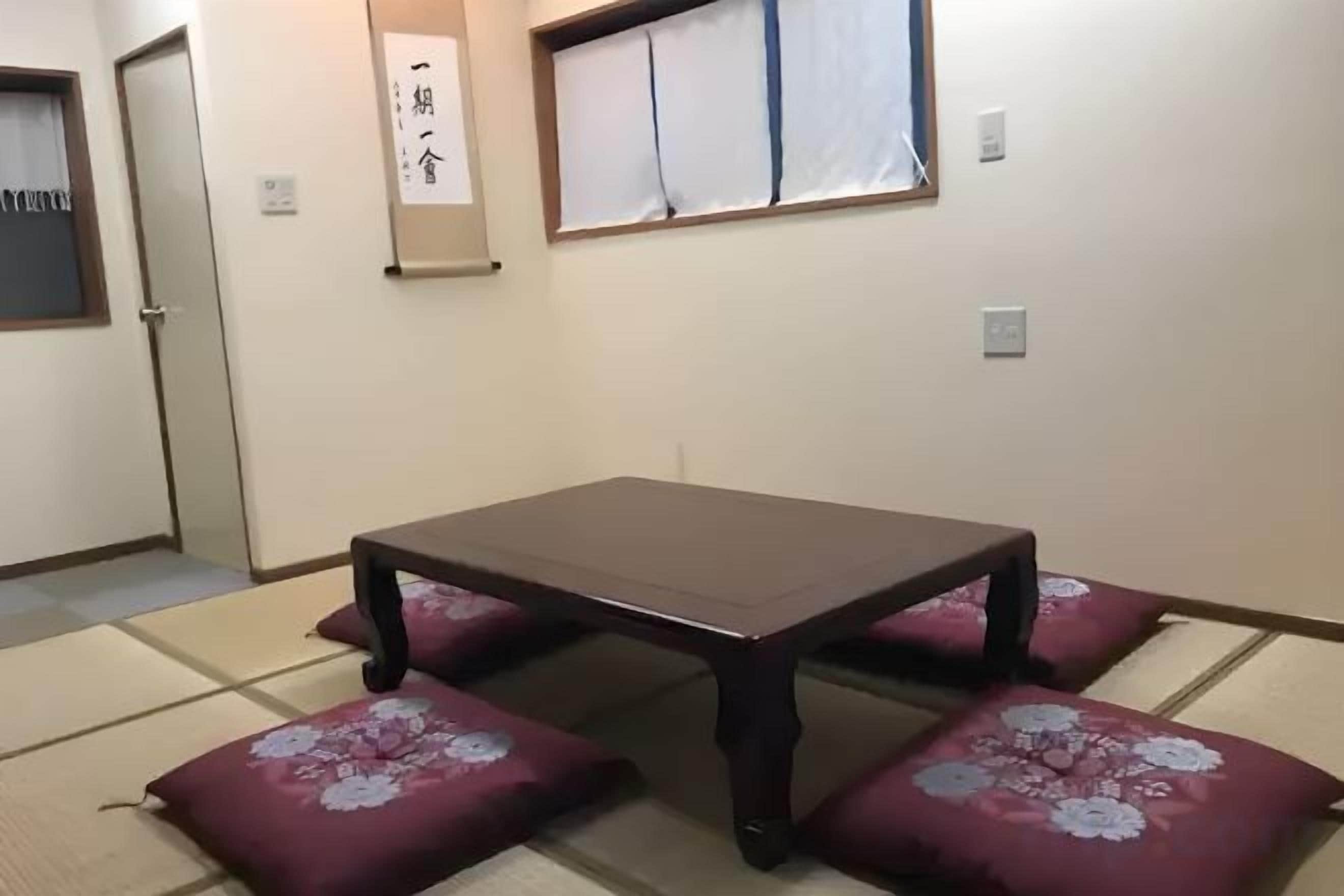 Une pièce de style japonais traditionnel, avec un sol recouvert de tatamis, une petite table basse entourée de coussins et un paravent en papier de riz (shoji).