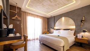A hotel room with a bed, bedside table, lamp, chair, and a desk with a coffee maker. - Onomo Ain Sebaa (Casablanca)