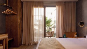A hotel room with a large bed, wooden furniture, a balcony with a chair, and a view of greenery outside. - Onomo Ain Sebaa (Casablanca)
