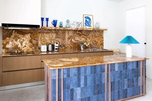A kitchen with a marble backsplash, wooden cabinets, and a blue-tiled island.