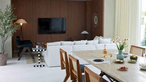 A modern living room with a sofa, dining table, chairs, a TV, and a potted plant. - Prime Beach House No. V7 (Sattahip)