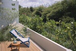 A balcony with a lounge chair and a small table, surrounded by dense greenery.