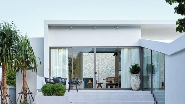 A modern building with a staircase leading to a glass door entrance, surrounded by potted plants and outdoor furniture. - Prime Beach House No. V7 (Sattahip)