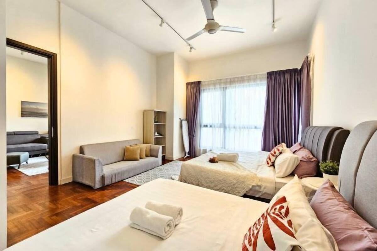 Ein Hotelzimmer mit einem Bett, zwei Sofas, einem Deckenventilator, einem Fenster mit Vorhängen und einem kleinen Bücherregal.