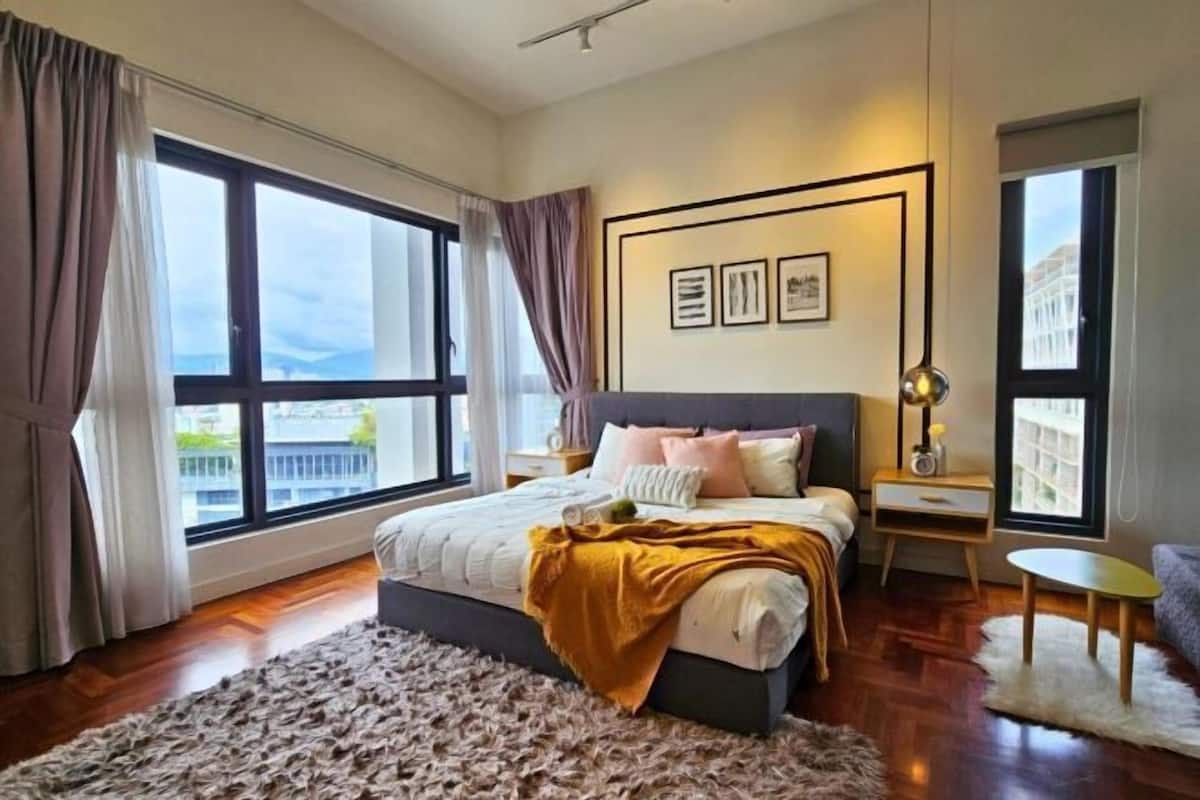 Ein modernes Schlafzimmer mit einem großen Bett, einem Nachttisch, einer Lampe und Blick auf die Stadt durch große Fenster.