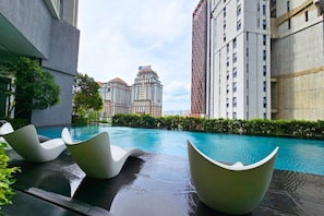 A swimming pool with modern chairs, surrounded by high-rise buildings.