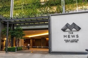 La entrada a The Mews Kuala Lumpur City Centre, con un diseño moderno que incluye una cubierta de vidrio y un logotipo destacado.