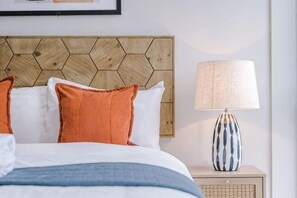 A neatly made bed with white and orange pillows, a blue blanket, and a wooden headboard with a geometric pattern. - Host & Stay The Baltic Penthouse 2 (Liverpool)