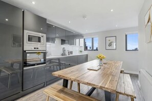 A modern kitchen with a wooden table and bench, a refrigerator, and a microwave. - Host & Stay The Baltic Penthouse 2 (Liverpool)