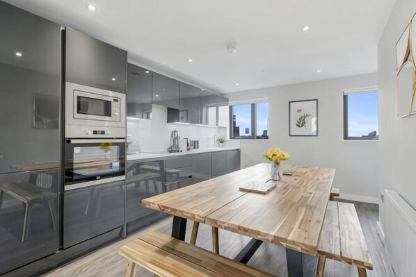 A modern kitchen with a wooden table and bench, a refrigerator, and a microwave. - Host & Stay The Baltic Penthouse 2 (Liverpool)