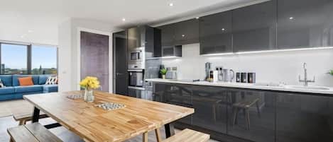 A modern kitchen with dark cabinets, a wooden dining table, and a city view.