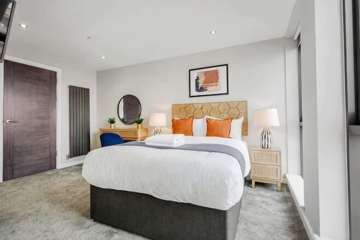 A modern hotel room with a large bed, a wooden headboard, two bedside tables with lamps, and a large window.
