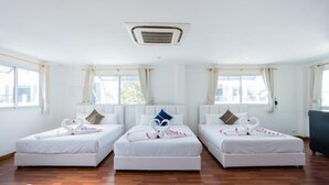 Habitación de hotel con tres camas individuales, un ventilador de techo y amplias ventanas.