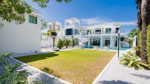 A modern building with a pool, surrounded by a well-maintained lawn and palm trees. - Modern 5BR Party Gathering Pool Villa - VVP31.10 (Pattaya)