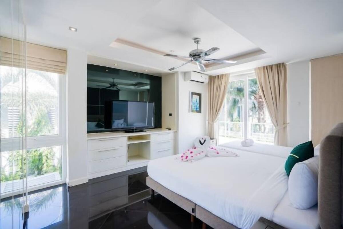 Habitación de hotel moderna con una cama grande, televisión, ventilador de techo y vista a zonas verdes.