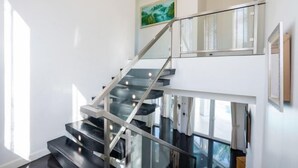 A modern interior with a glass staircase, a painting on the wall, and a large window. - Modern 5BR Party Gathering Pool Villa - VVP31.10 (Pattaya)