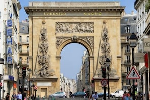 A historic archway with inscriptions, surrounded by urban buildings and street signs.