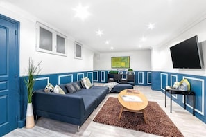 A modern living room with a sectional sofa, a coffee table, a flat-screen TV, and a kitchen area in the background. - Elegant 130m² Apartment in Central Paris, Marais (Paris)