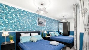 Une chambre avec deux lits, une table de chevet, une lampe, une plante en pot et un mur orné d’un motif de feuilles.