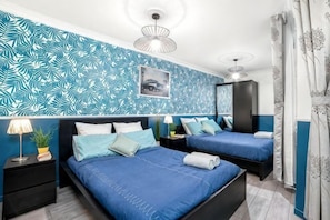 A bedroom with two beds, a nightstand, a lamp, a potted plant, and a wall with a leaf pattern.