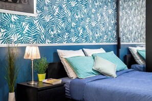 Un dormitorio con cama, almohadas, una mesita de noche, lámpara y pared decorada con un diseño de hojas.