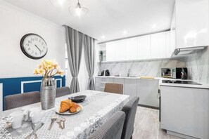 Een moderne keuken met witte kasten, een marmeren spatwand en een eethoek met een tafel gedekt voor twee personen.
