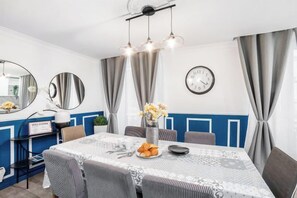 Een eetgedeelte met een tafel voor vier personen, een klok aan de muur en een spiegel boven de tafel.