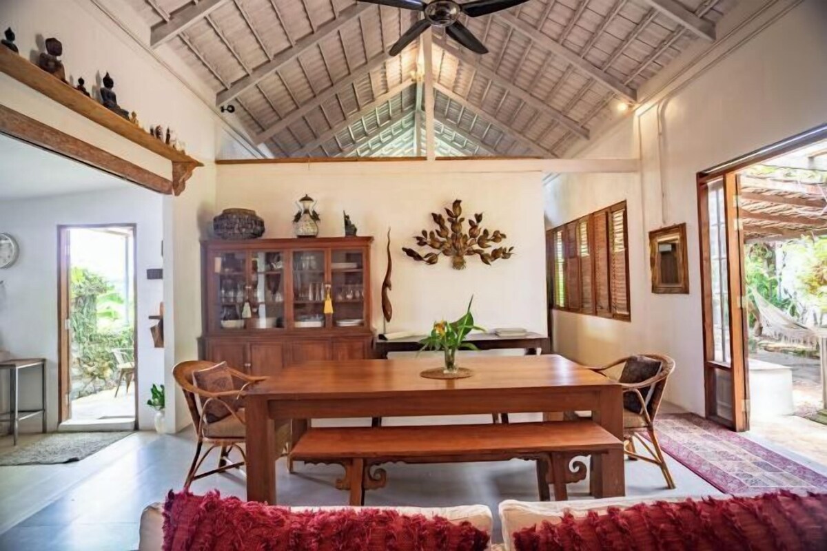 A spacious dining area with a wooden table and chairs, a ceiling fan, and a view of the outdoors.