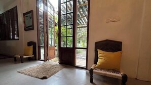 A room with a wicker chair with a yellow cushion, a wooden bench, and a large glass door leading outside. - Hermoso Hideaway (Klaeng)