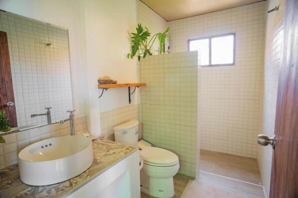 Un baño con lavamanos blanco, inodoro y zona de ducha.
