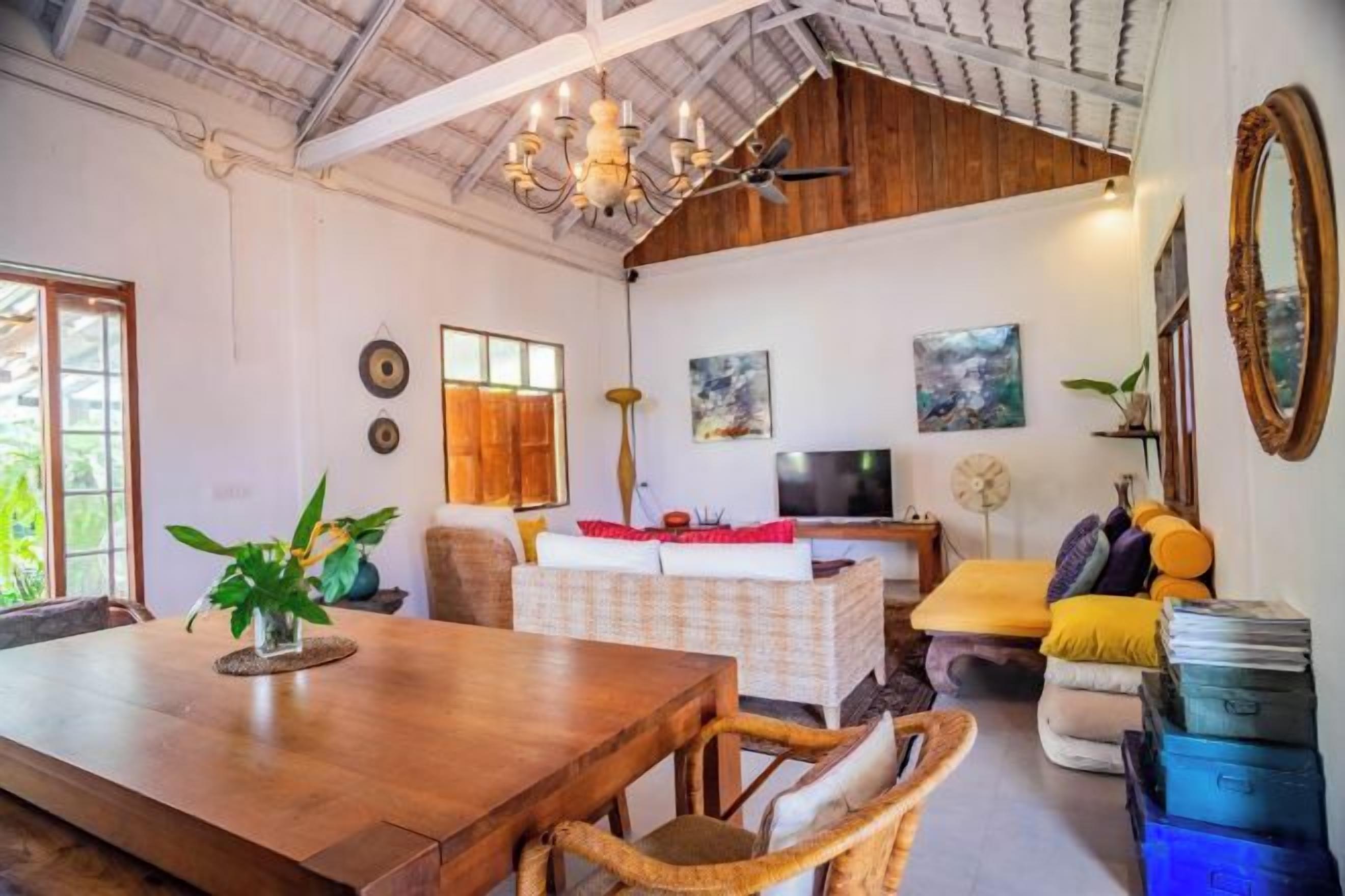 A spacious living area with a wooden dining table, comfortable seating, a television, and a large mirror.