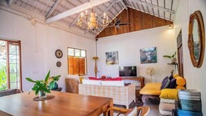 A spacious living area with a wooden dining table, wicker chairs, a sofa, and a television. - Hermoso Hideaway (Klaeng)
