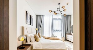 Quarto de hotel com cama, luminária, cortinas, candelabro e cômoda.